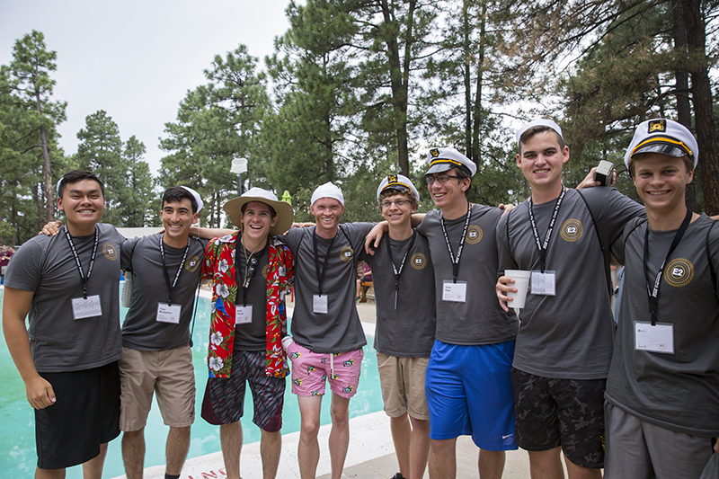 A group of young men campers, arm in arm, stand next to the pool posed smiling for the photo.