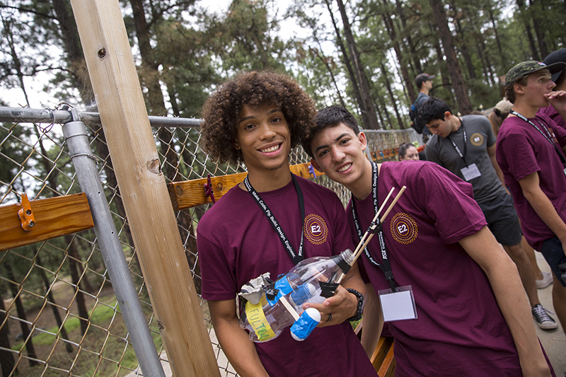 Two campers, young men, stand together for the camera while holding a duct-tape and recyclables creation.